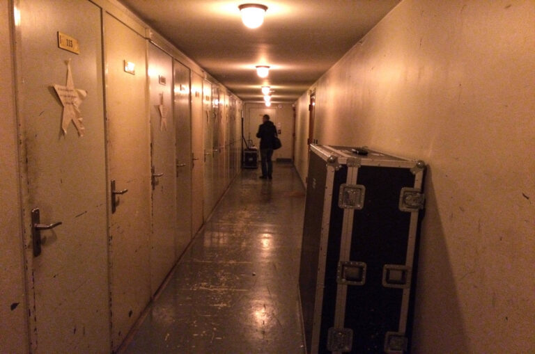 Le couloir des loges d’une salle de concert, portes numérotées sous les ampoules