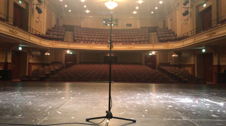 Une salle de concert vide vue depuis la scène, fosse et gradins sous les lumières de service